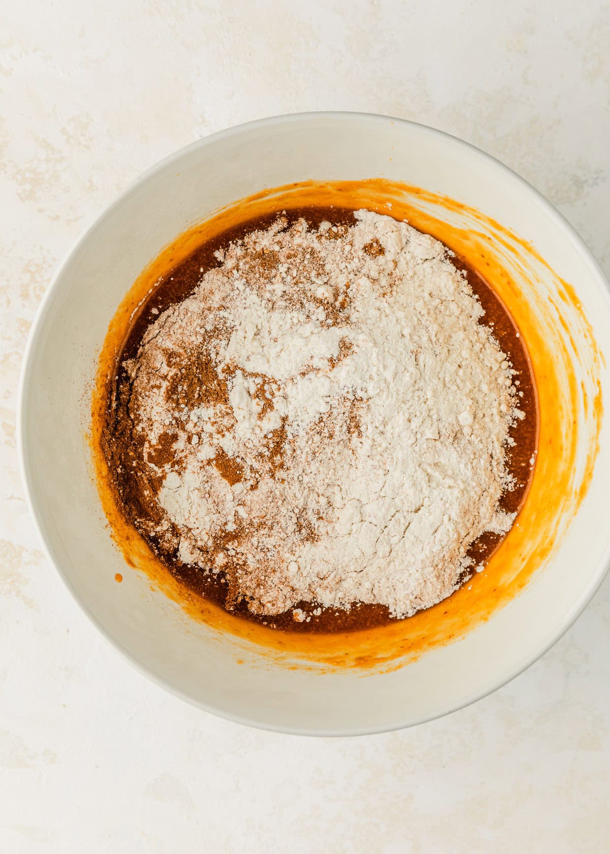 A white bowl of pumpkin filling, flour, and spices on a beige table.