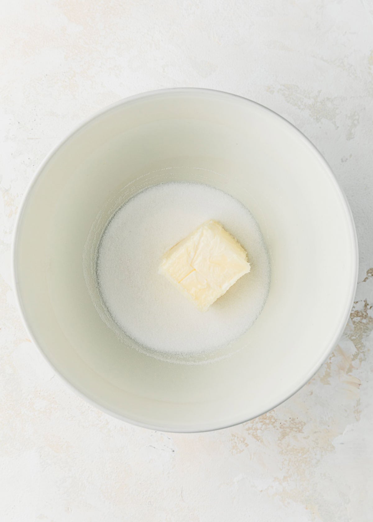A white bowl of butter and sugar on a white counter.