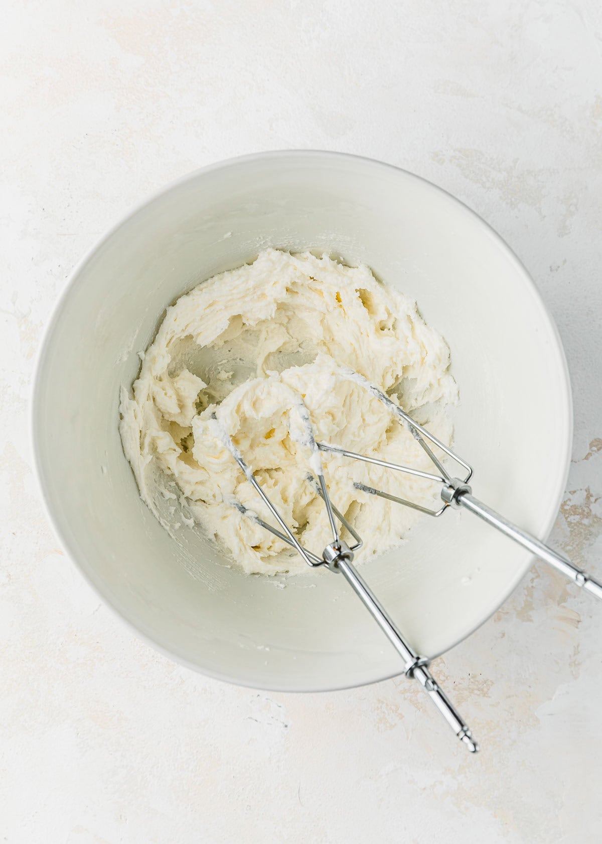 A white bowl of whipped butter and sugar with beaters.
