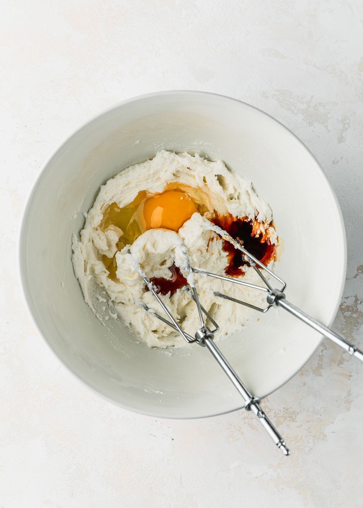 A white bowl of whipped butter and sugar, an egg, and vanilla.