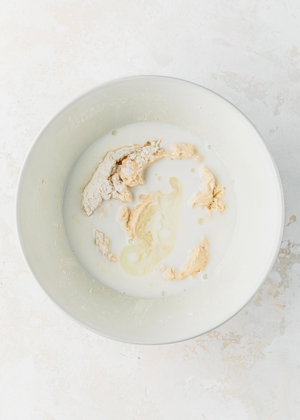 A white bowl of cupcake batter with buttermilk on a white counter.