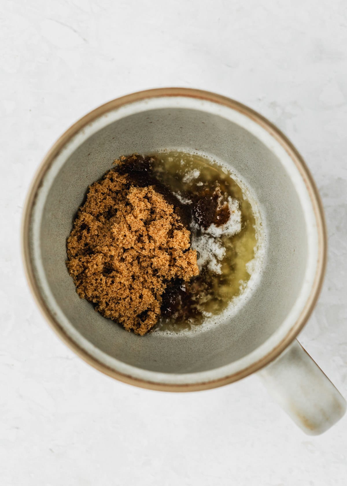 A grey mug with butter and brown sugar on a white counter.
