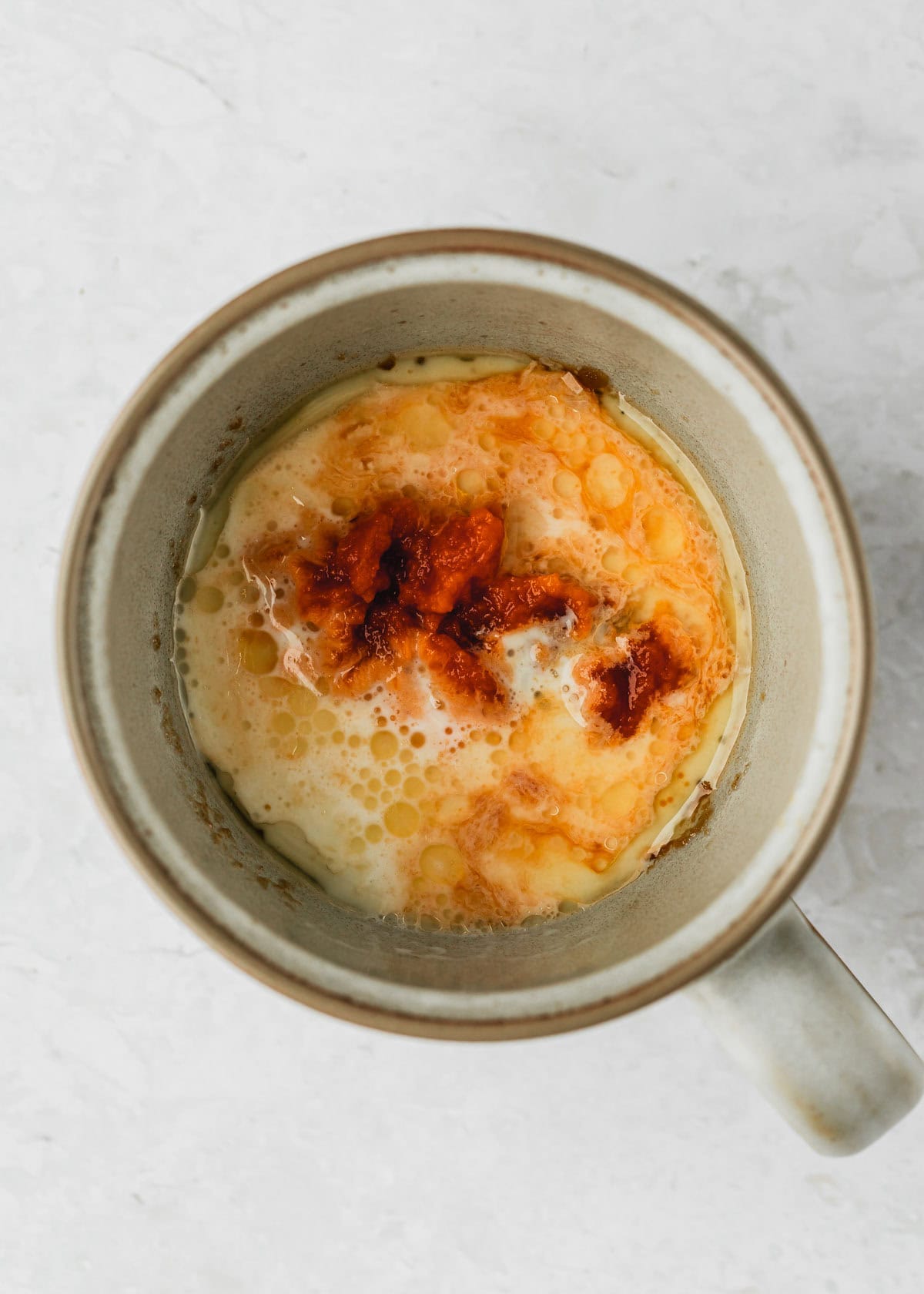 A grey mug of butter, sugar, pumpkin, milk, and vanilla for a pumpkin mug cake.