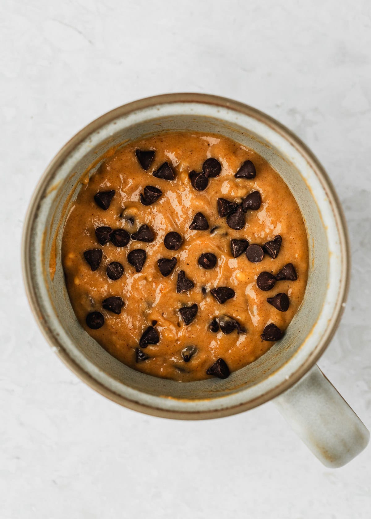 A raw pumpkin mug cake with chocolate chips on a white counter.