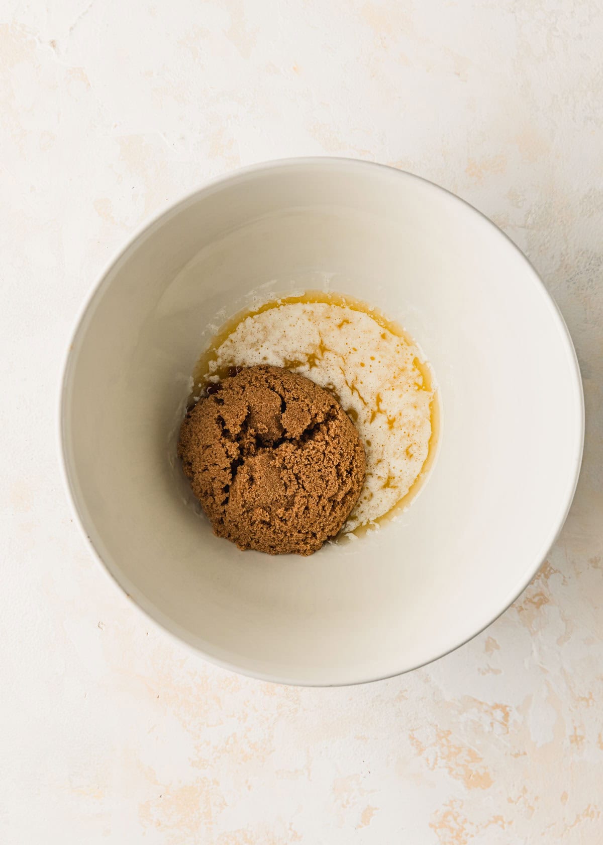 A white bowl of melted butter and brown sugar on a tan counter.