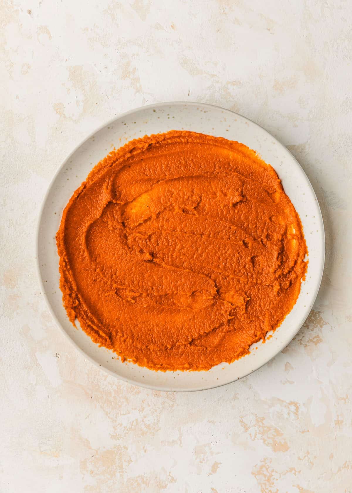 A white plate of pumpkin puree on a tan counter.