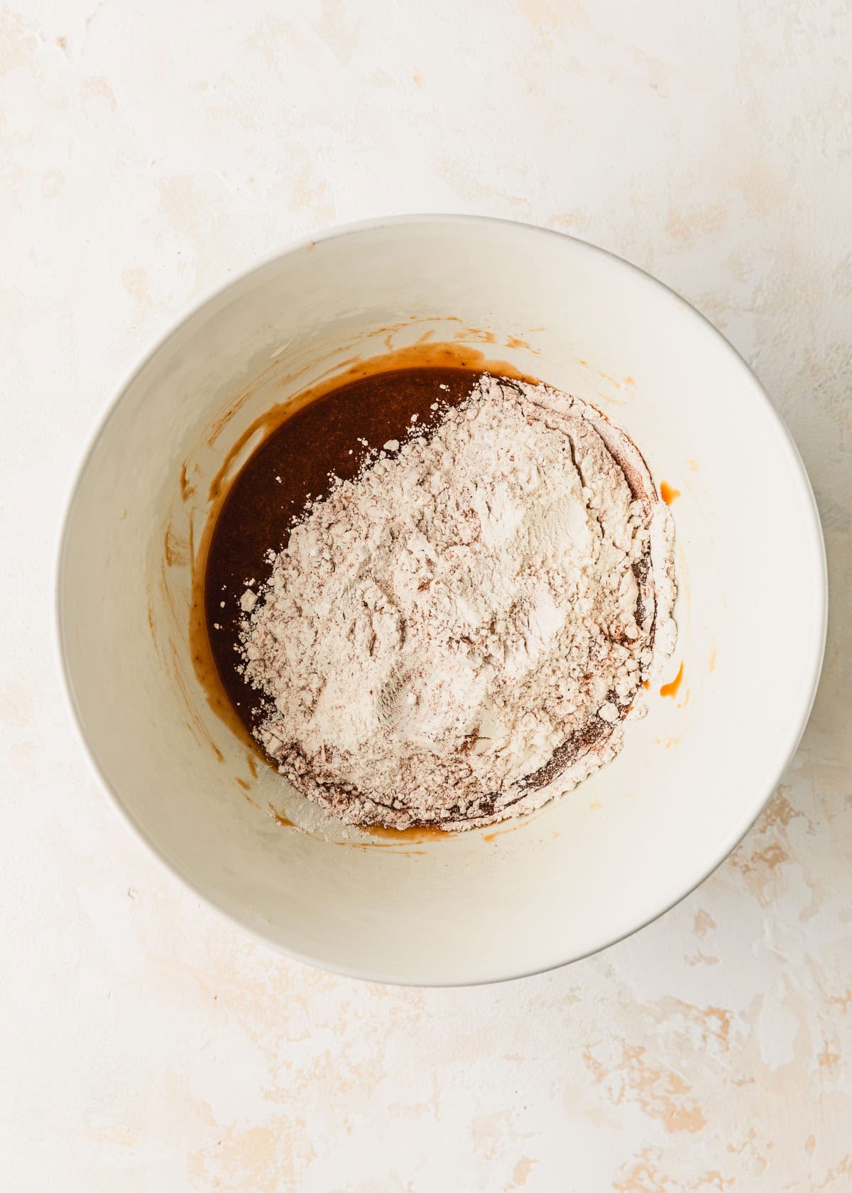 A white bowl of butter, sugar, eggs, pumpkin, and flour for small batch pumpkin cookies on a tan counter.