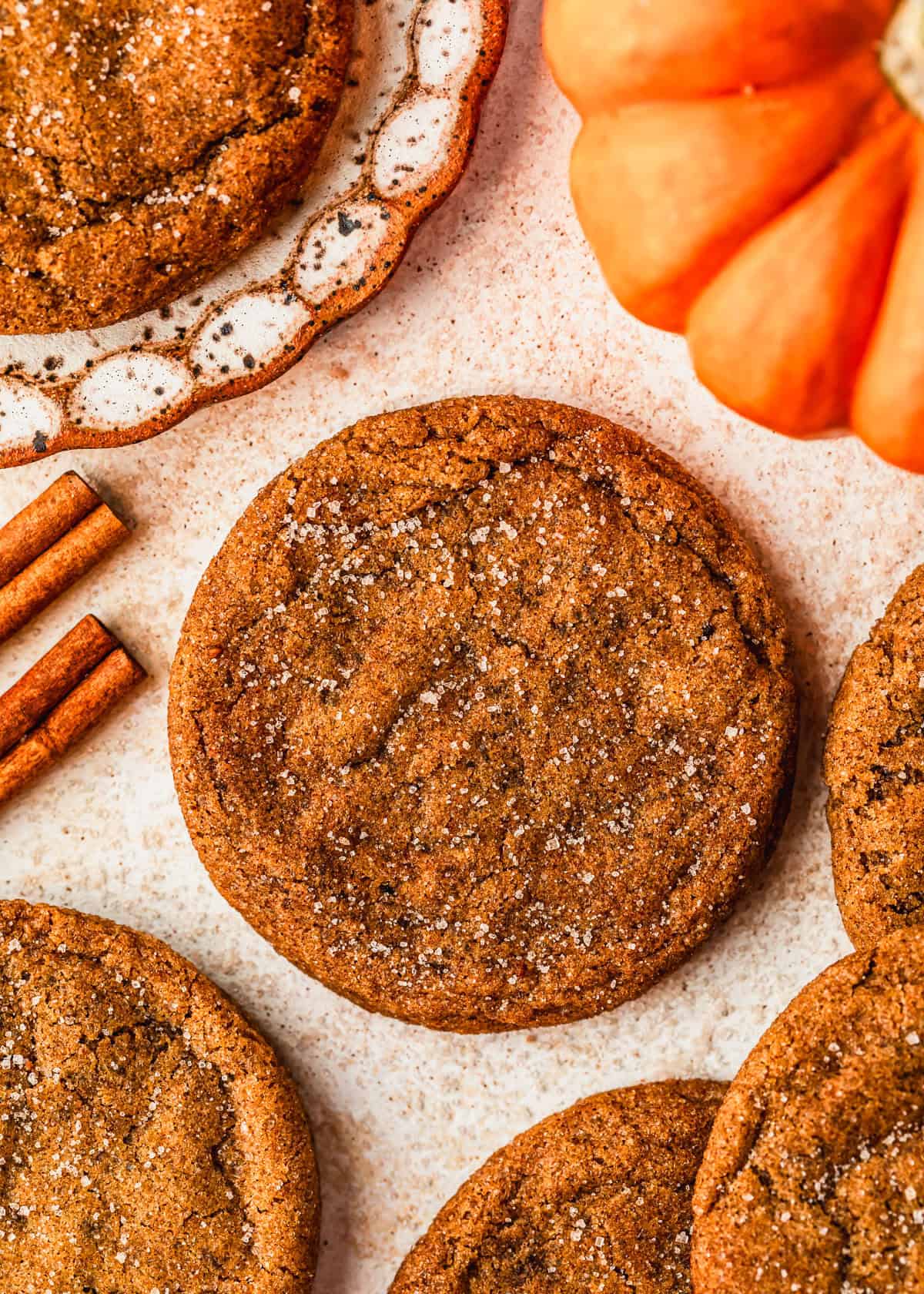 Rows of small batch pumpkin cookies on a tan counter next to a pumpkin, cinnamon sticks, and a white plate with a cookie on it.