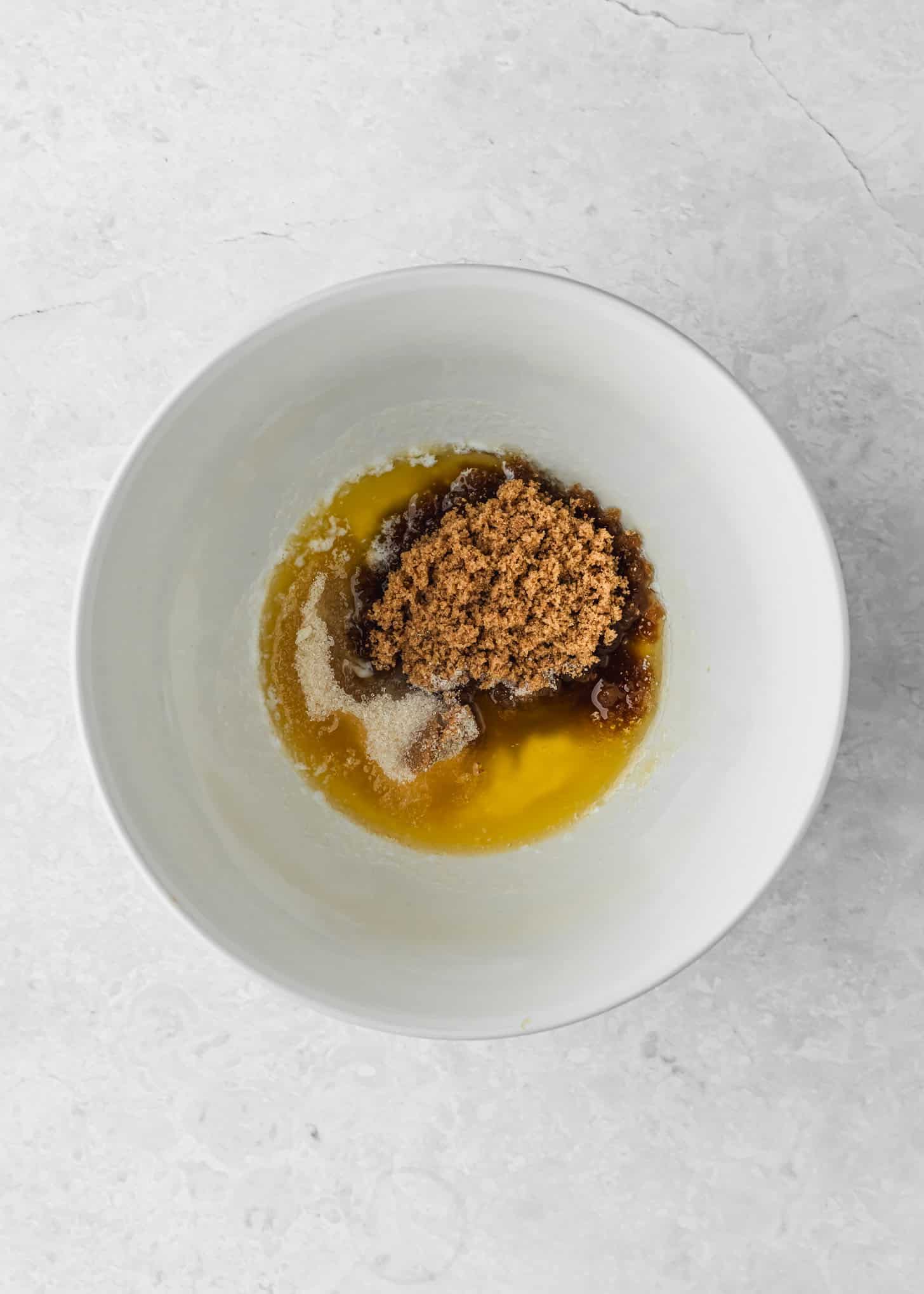 A white bowl of butter, sugar, and brown sugar on a white counter.