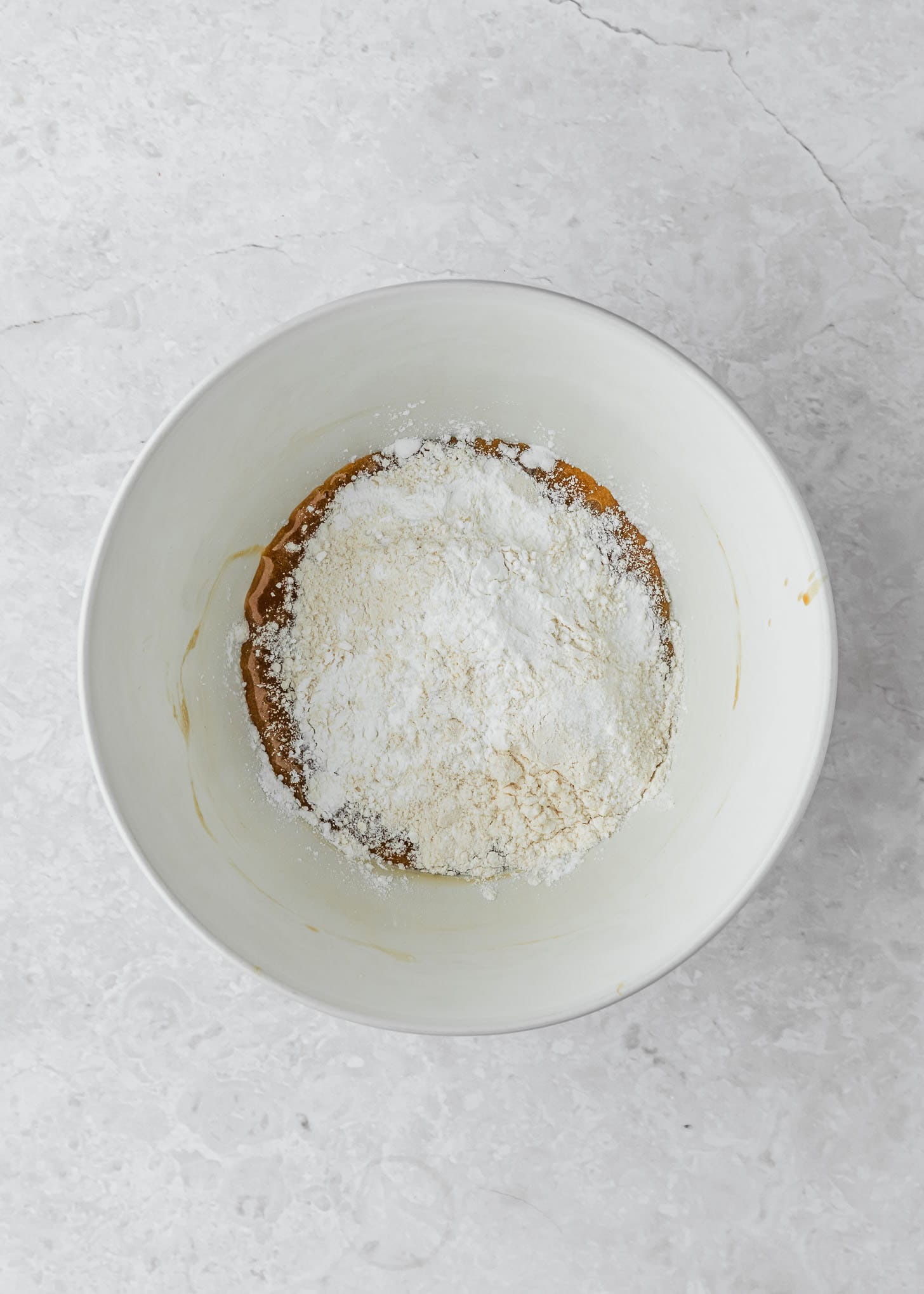 A white bowl of flour, sugar, butter, baking soda, and salt on a white counter.