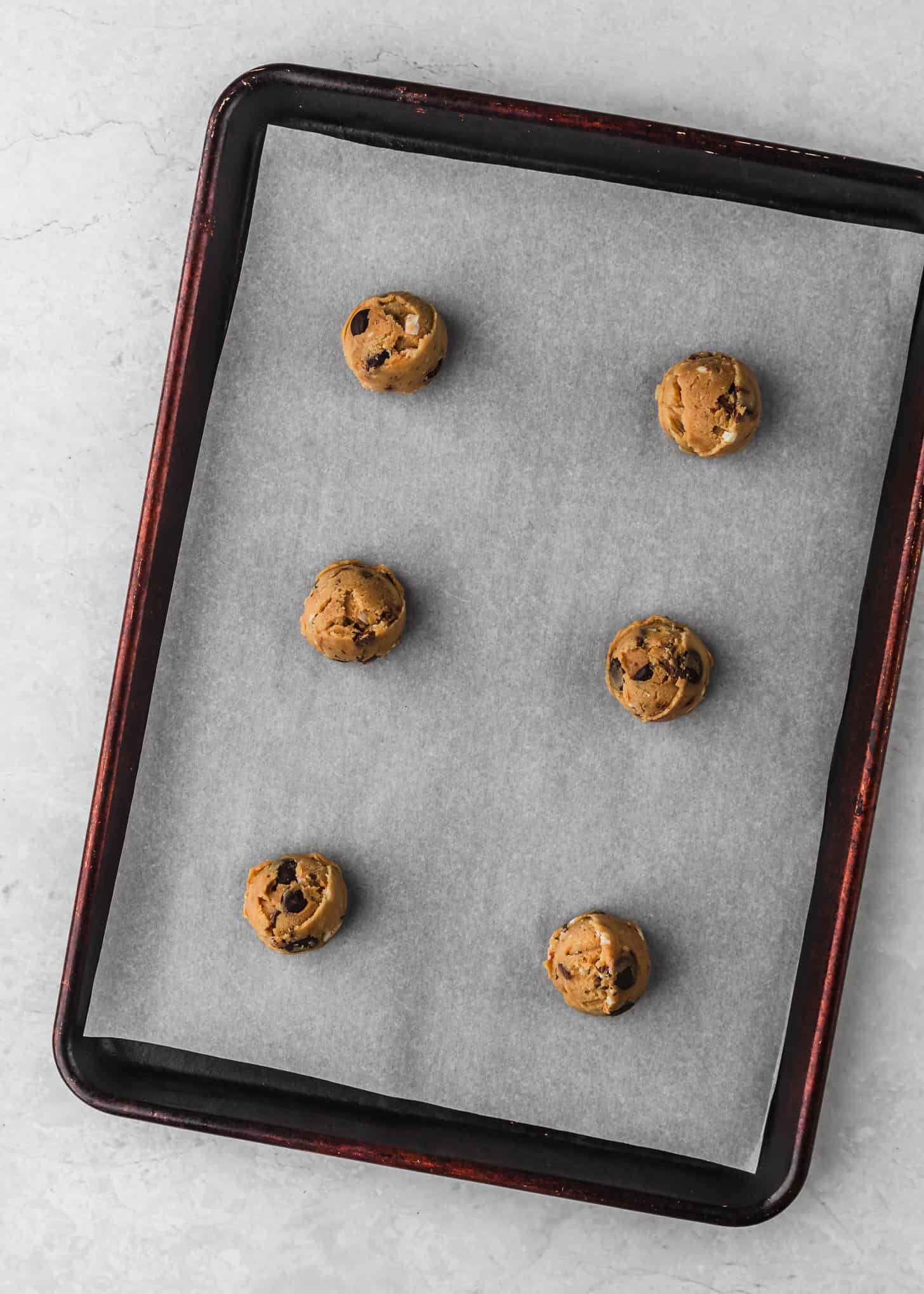 A sheet pan of raw small batch peppermint bark chocolate chip cookies on a white table.