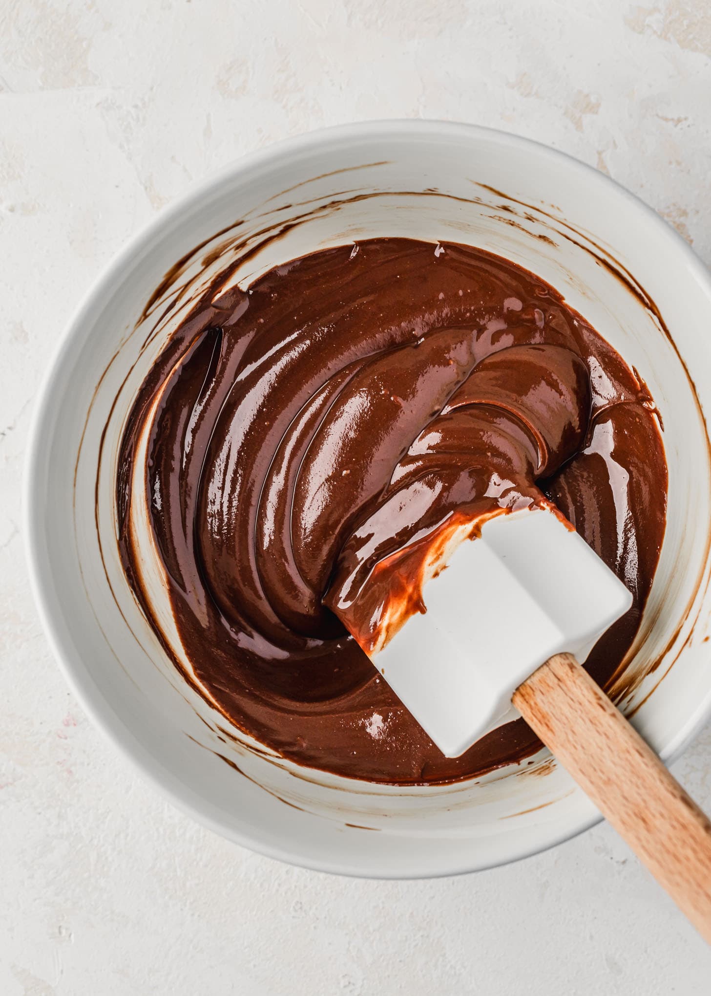 A white bowl of melted chocolate with a white rubber spatula.