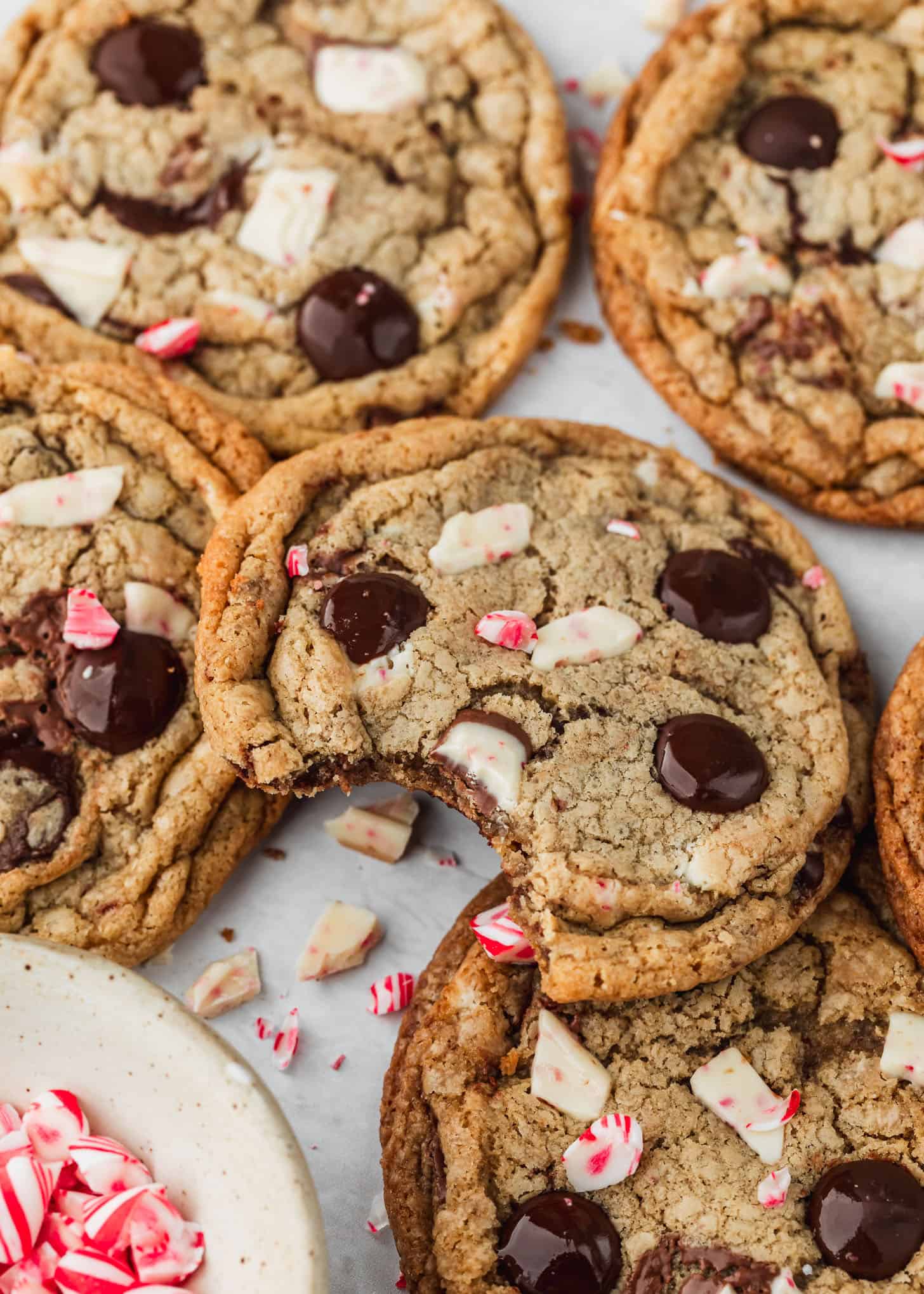 Rows of small batch peppermint bark chocolate chip cookies next to a white bowl of candy canes with a white background.