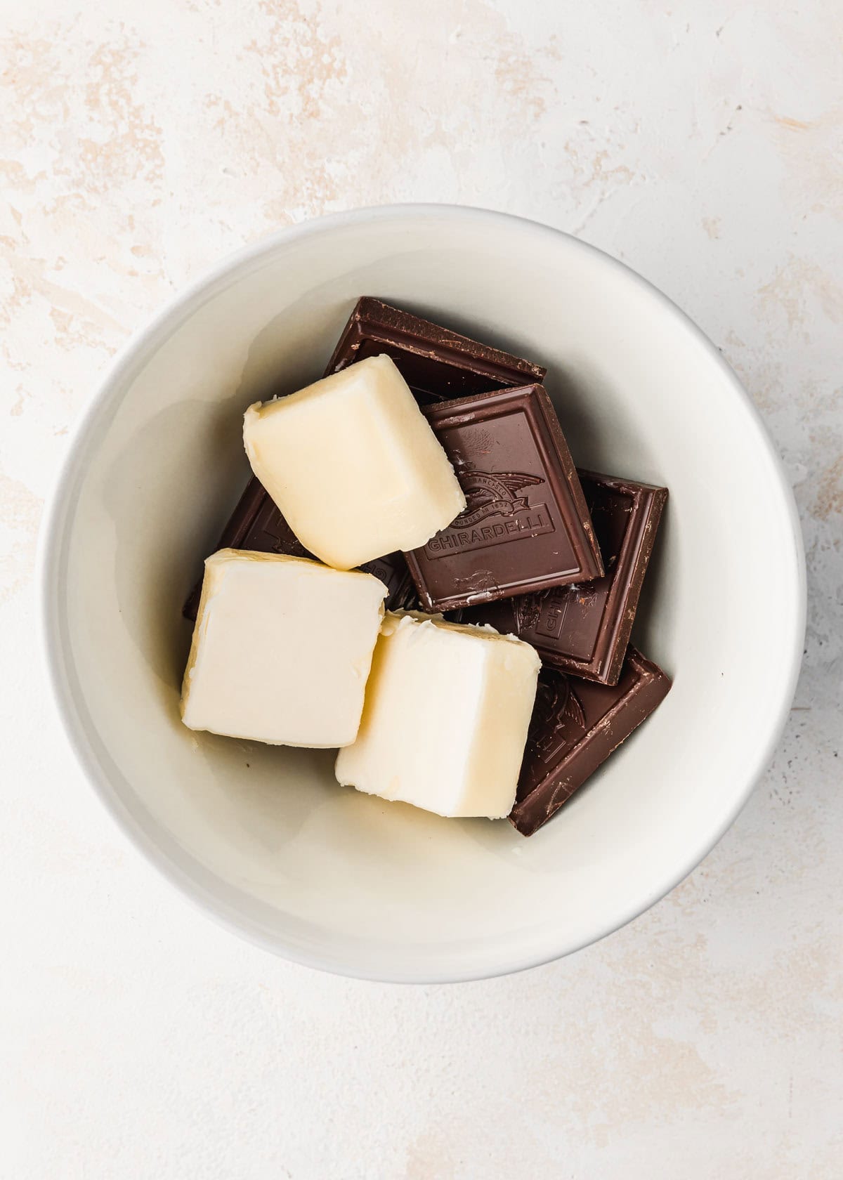 A white bowl of butter and chocolate on a beige table.