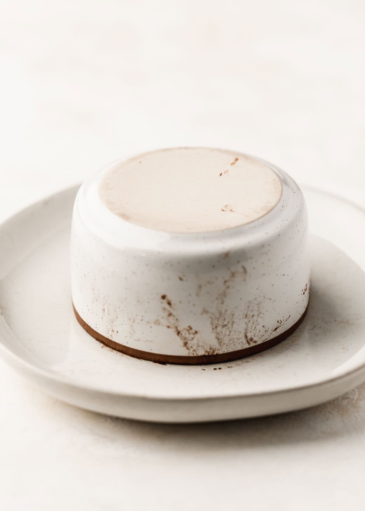 A white ramekin upside down on a white plate.