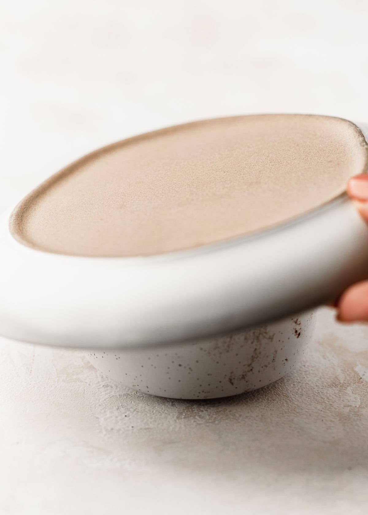 A hand placing a white plate on a white ramekin.