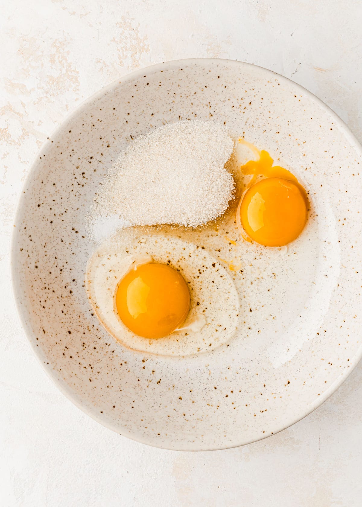 A white bowl of eggs and sugar on a white counter.