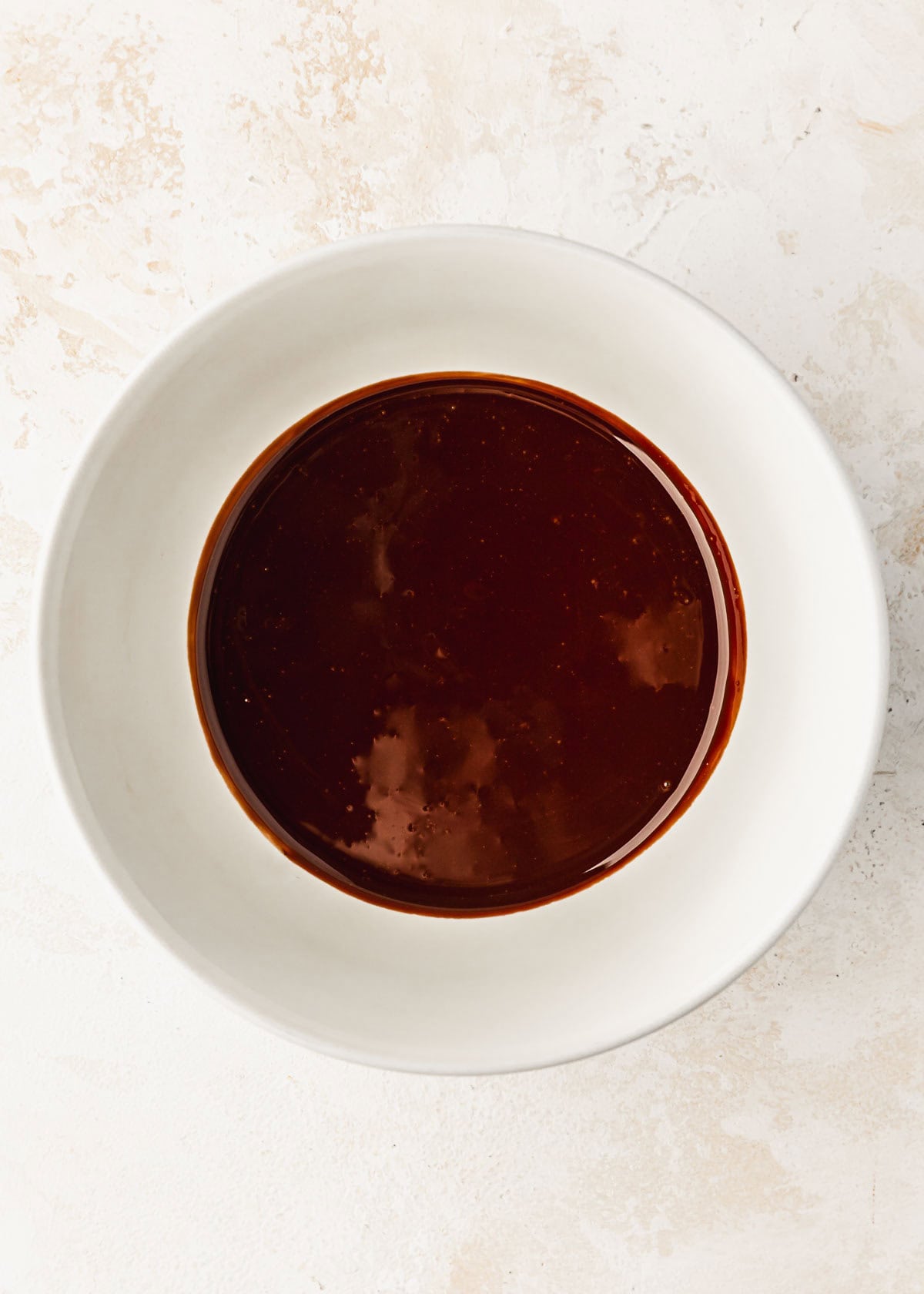 A white bowl of melted chocolate on a tan counter.