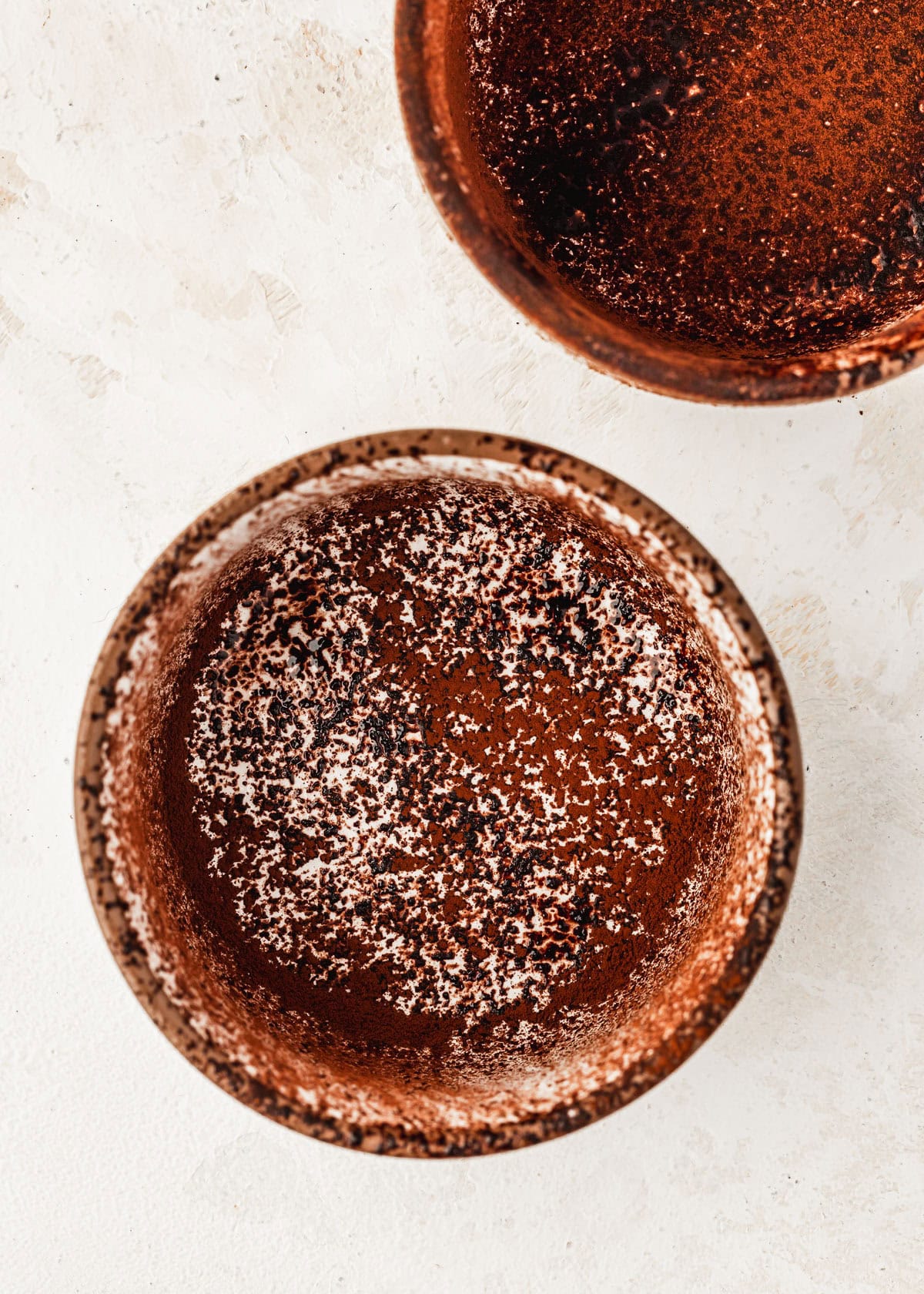 Ramekins dusted with cocoa powder on a beige table.