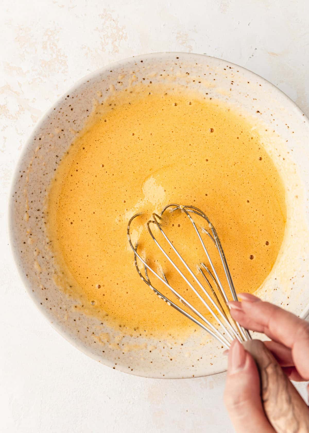 A hand whisking eggs and sugar in a white bowl.