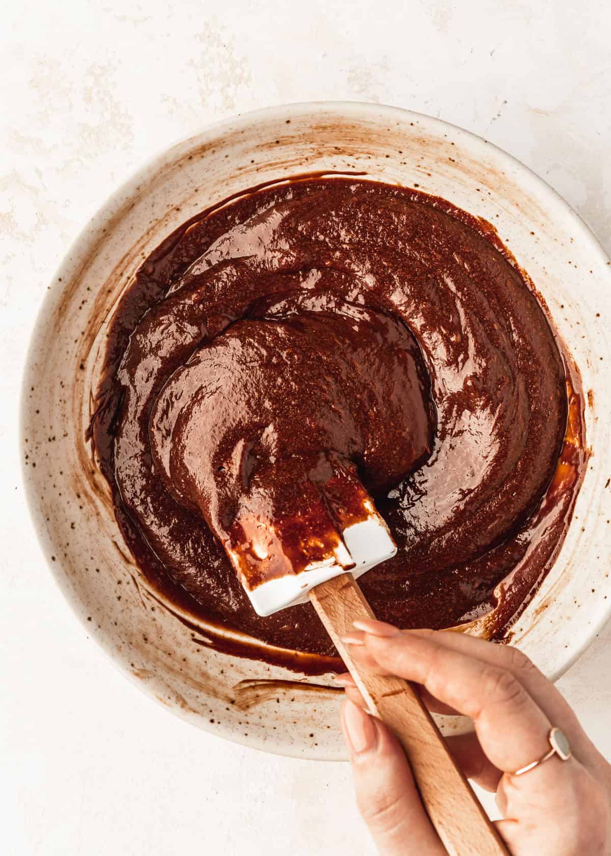 A hand using a rubber spatula to mix batter for lava cakes for two in a white bowl.
