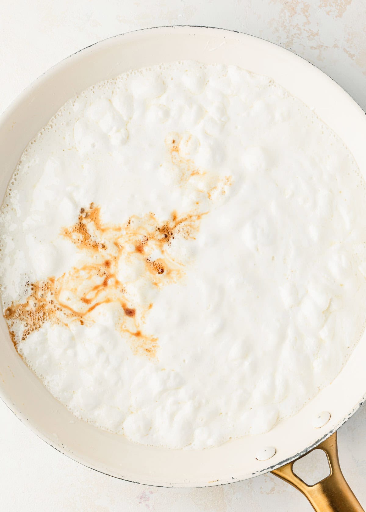 A white pan of melted marshmallows and vanilla on a tan counter.