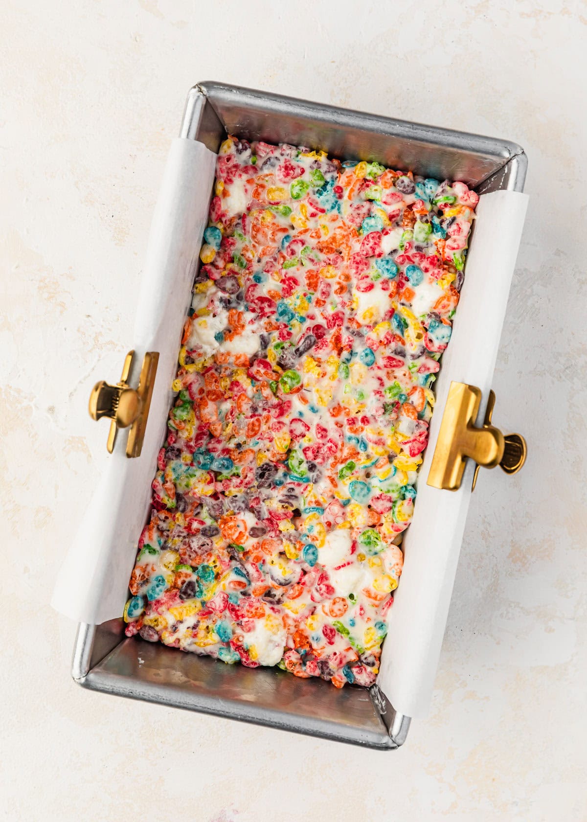 A loaf pan with Fruity Pebbles rice crispy treats on a tan counter.