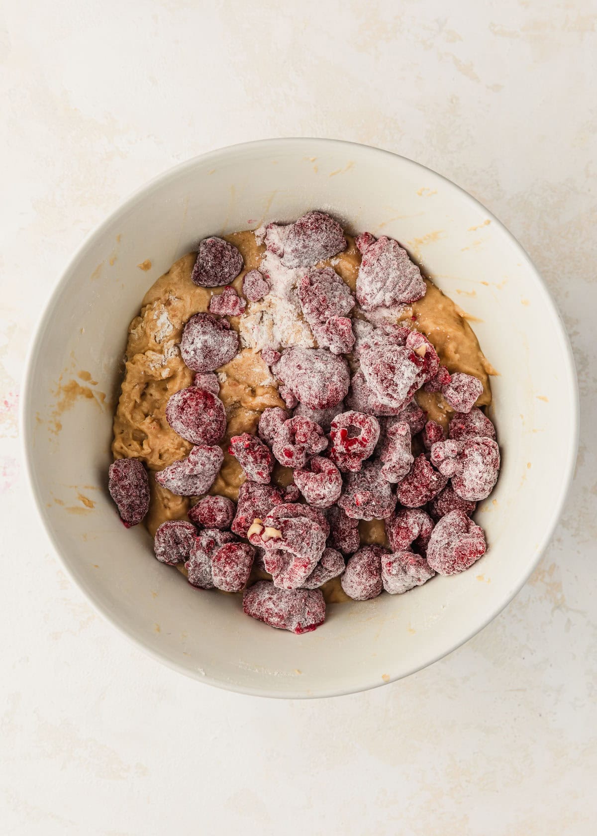 A white bowl of batter for small batch banana muffins topped with raspberries.
