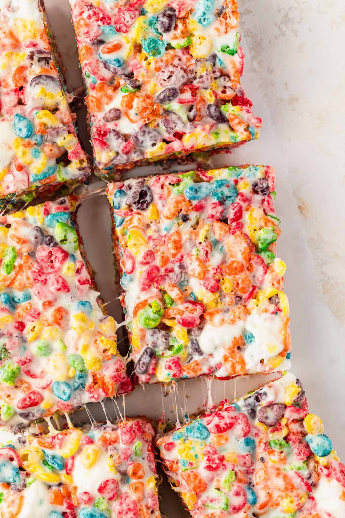 Rows of small batch Fruity Pebbles rice crispy treats on a tan and white speckled table.