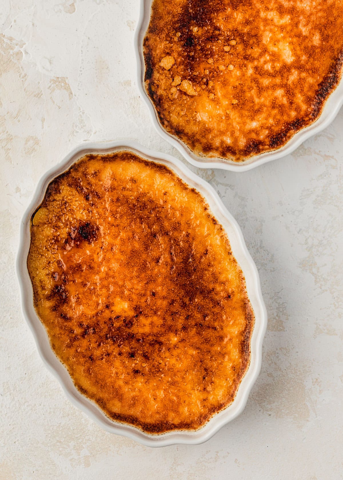 Two ramekins of crème brûlée on a white and beige counter.