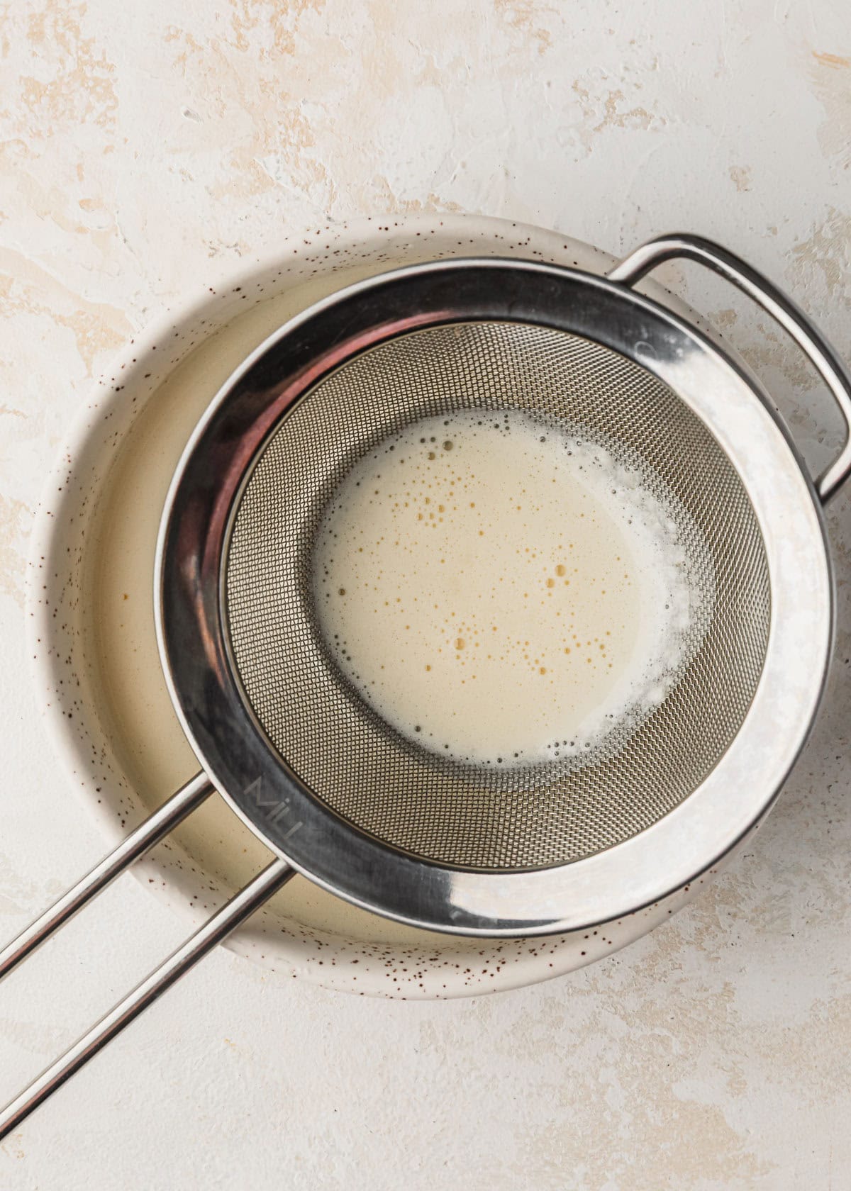 A sieve sifting custard into a white bowl.