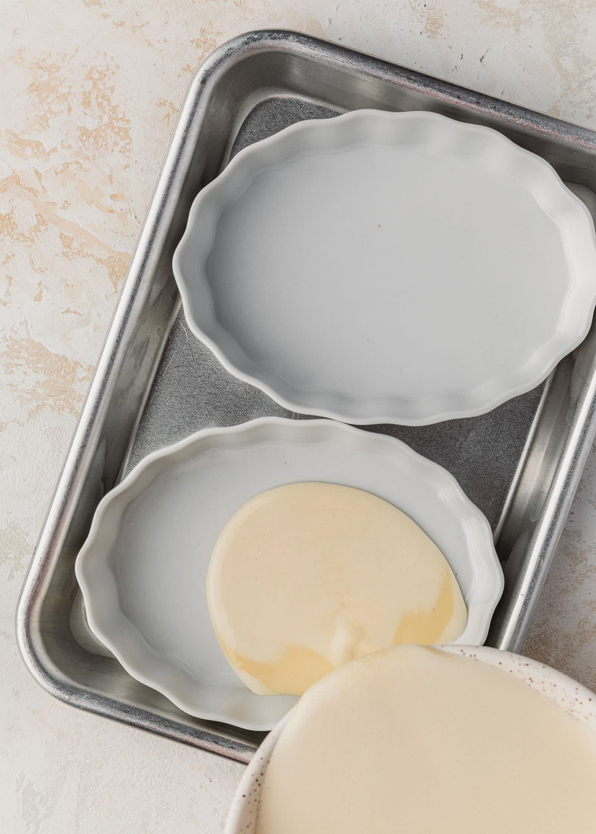 A bowl pouring creme brulee custard into two ramekins.