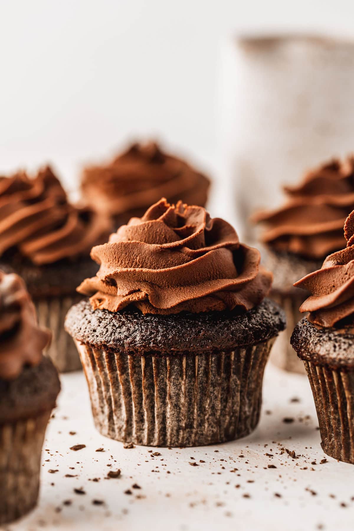Rows of small batch chocolate cupcakes next to a white pitcher on a white background.