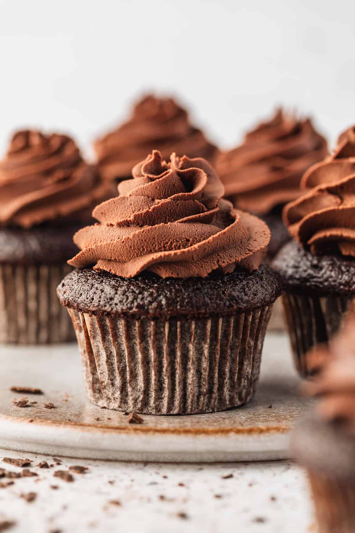 A grey platter of cupcakes topped with small batch whipped chocolate ganache with a white background.