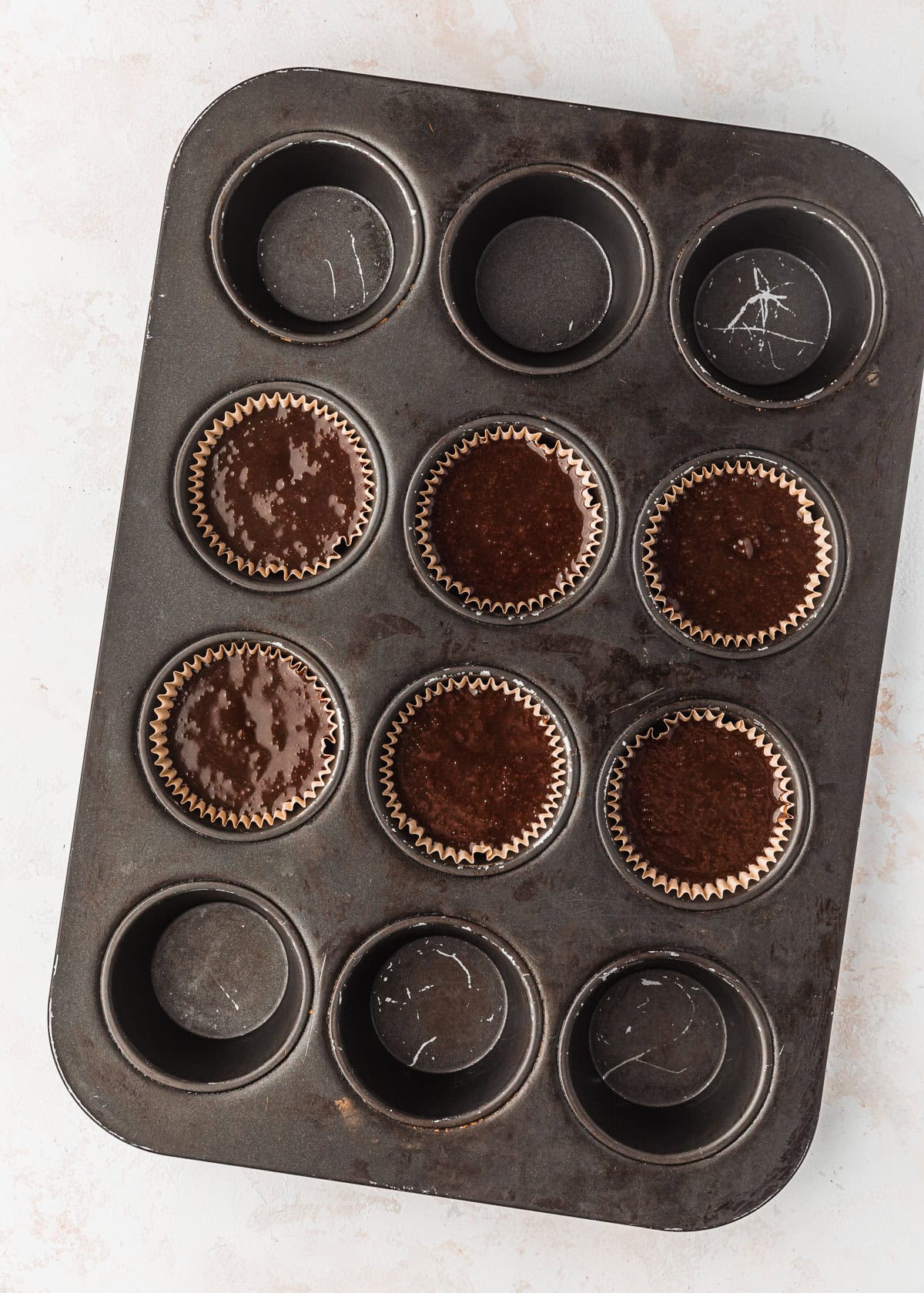 A pan of raw small batch chocolate cupcakes on a beige table.