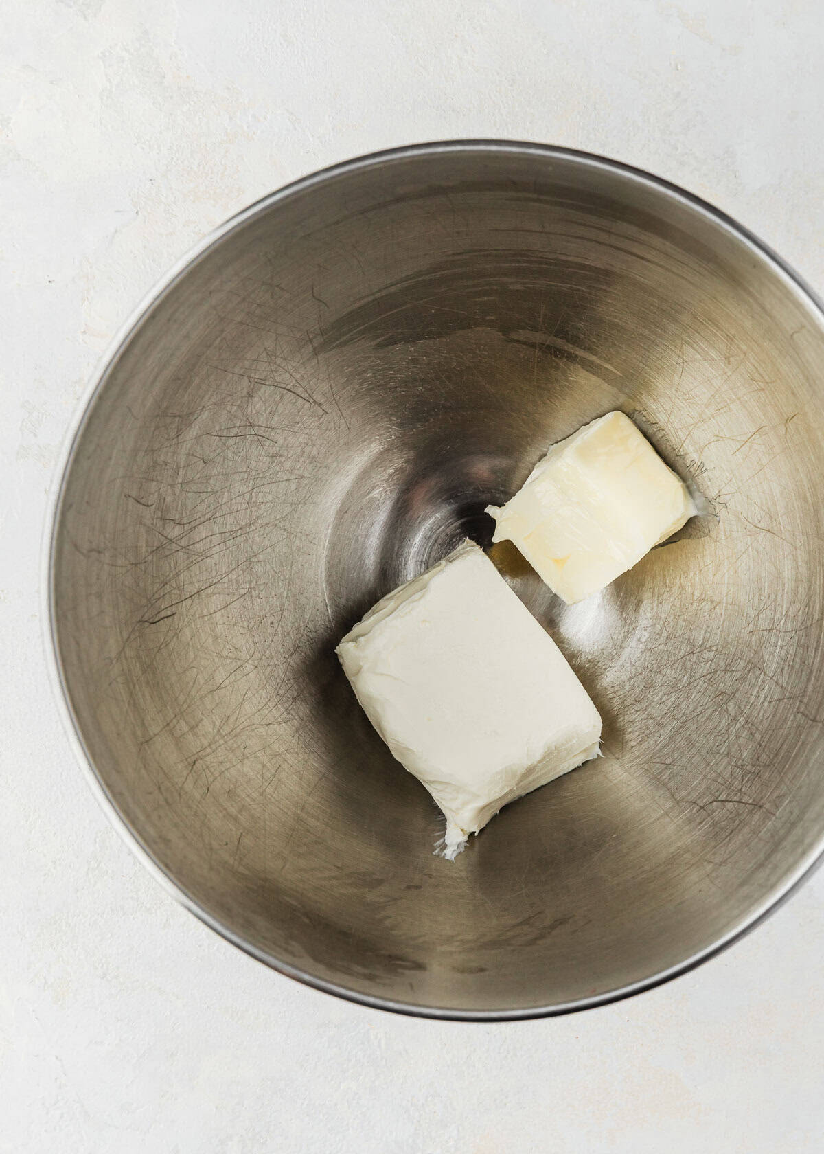 A silver bowl of butter and cream cheese on a white counter.