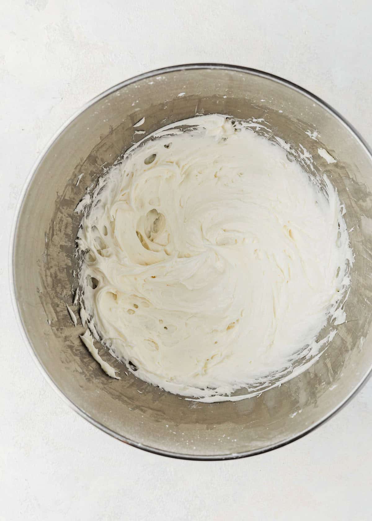 A silver bowl of small batch cream cheese icing on a white table.