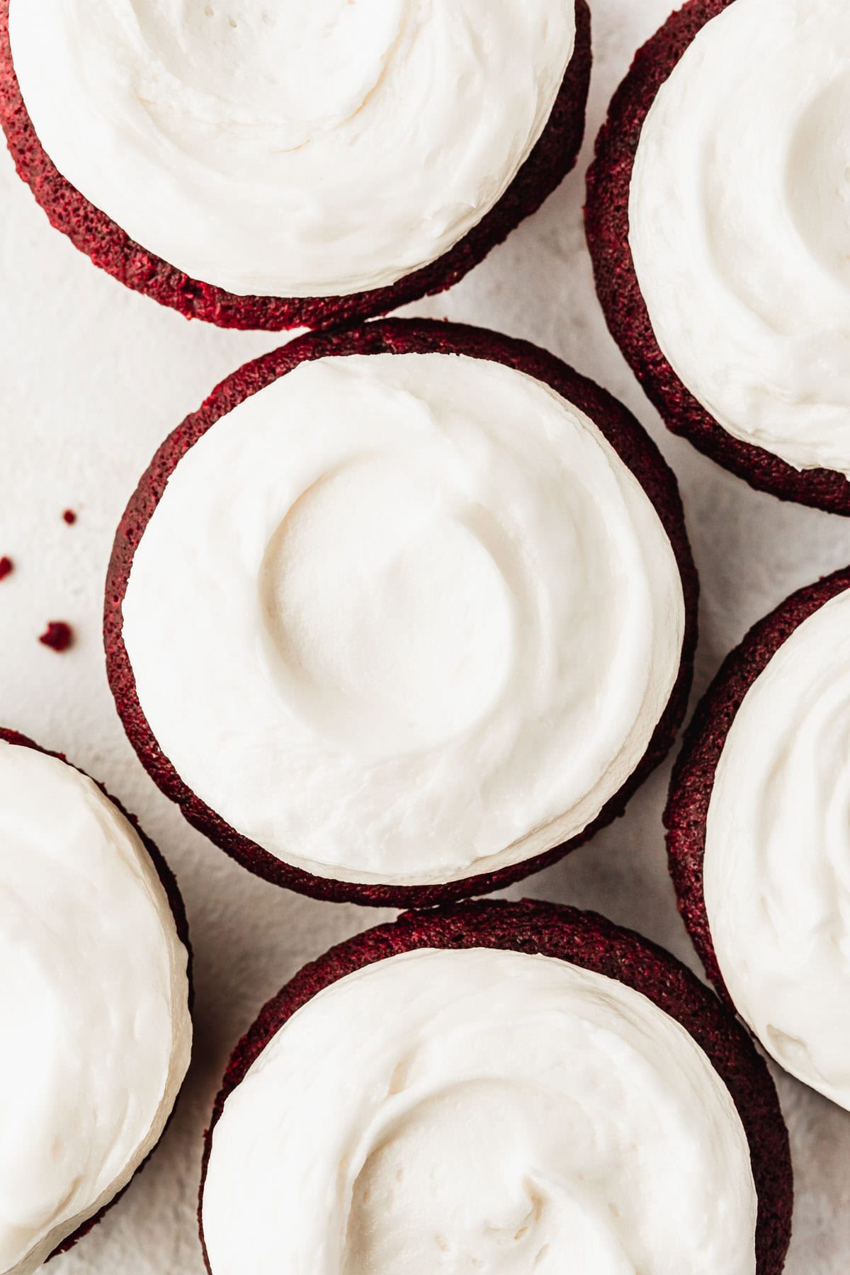 Rows of red velvet cupcakes topped with small batch cream cheese frosting on a white counter.