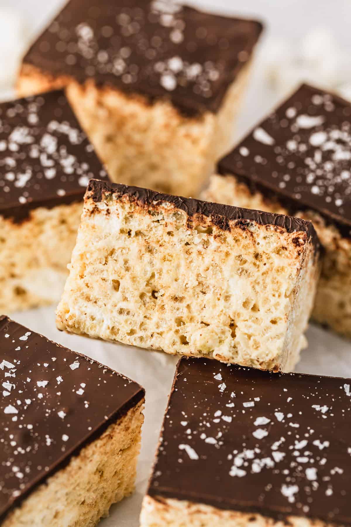 Rows of small batch chocolate covered Rice Krispie treats with flaky salt on parchment paper.