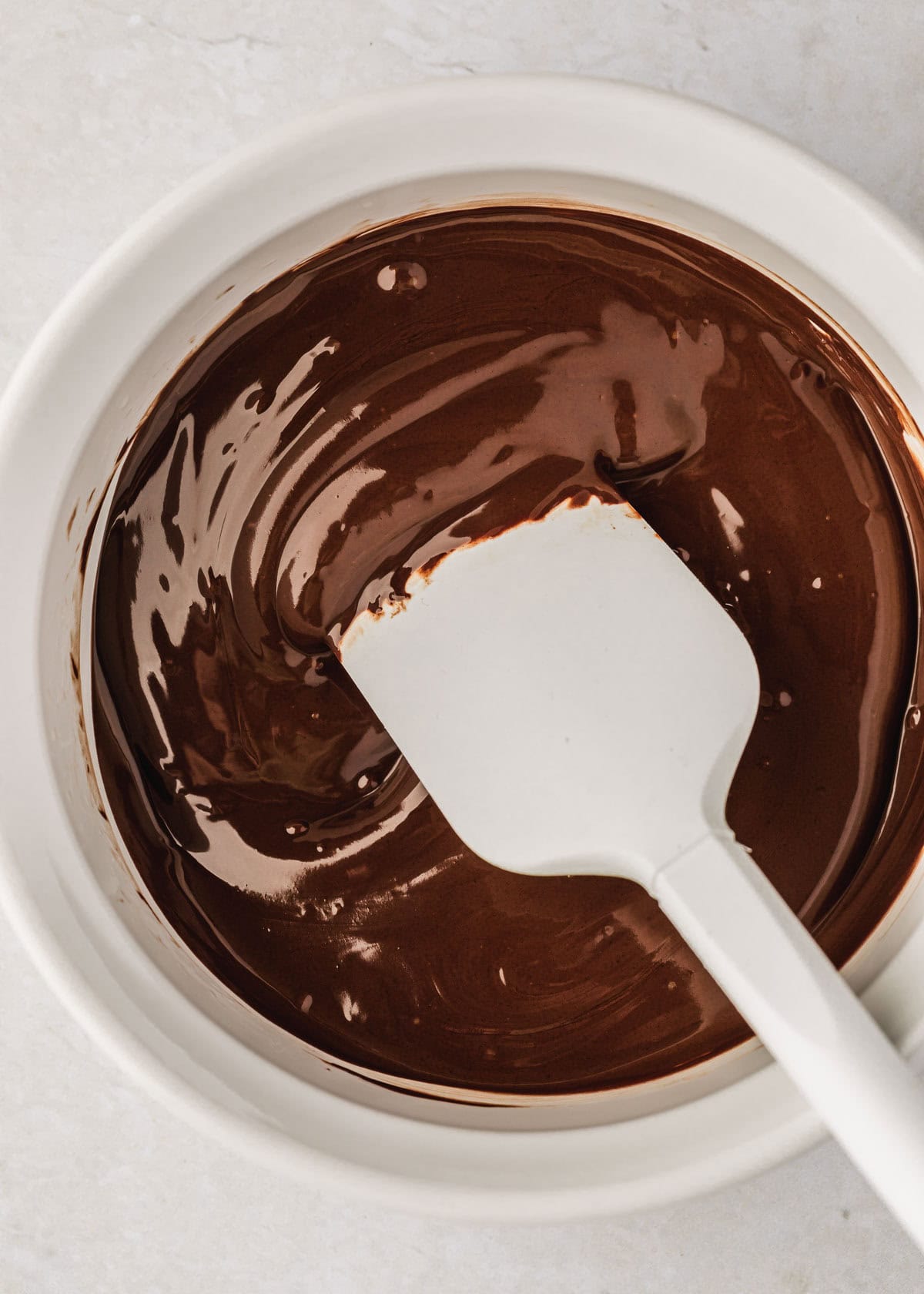 A white bowl of melted chocolate with a white rubber spatula.