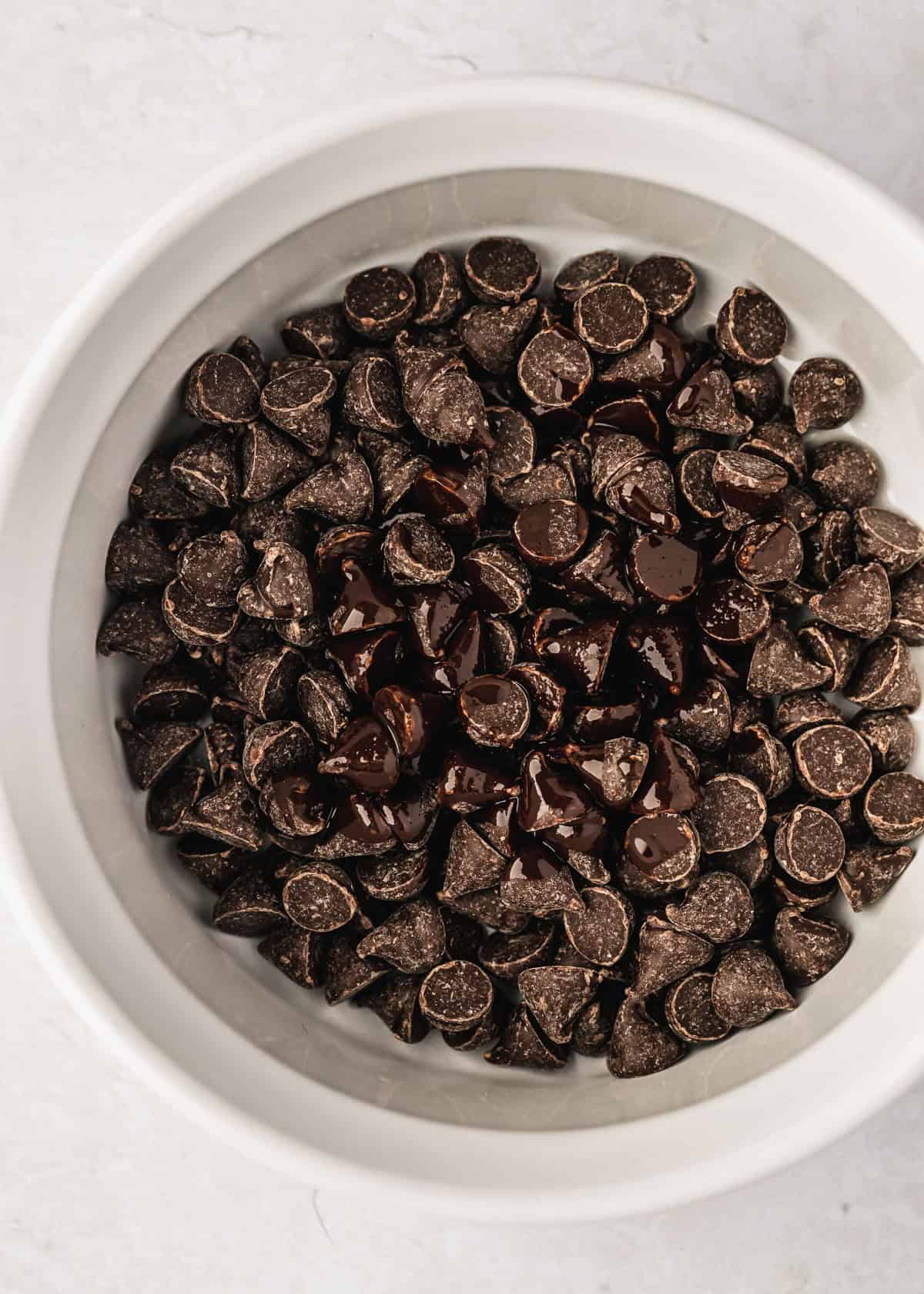 A white bowl of chocolate chips on a white counter.