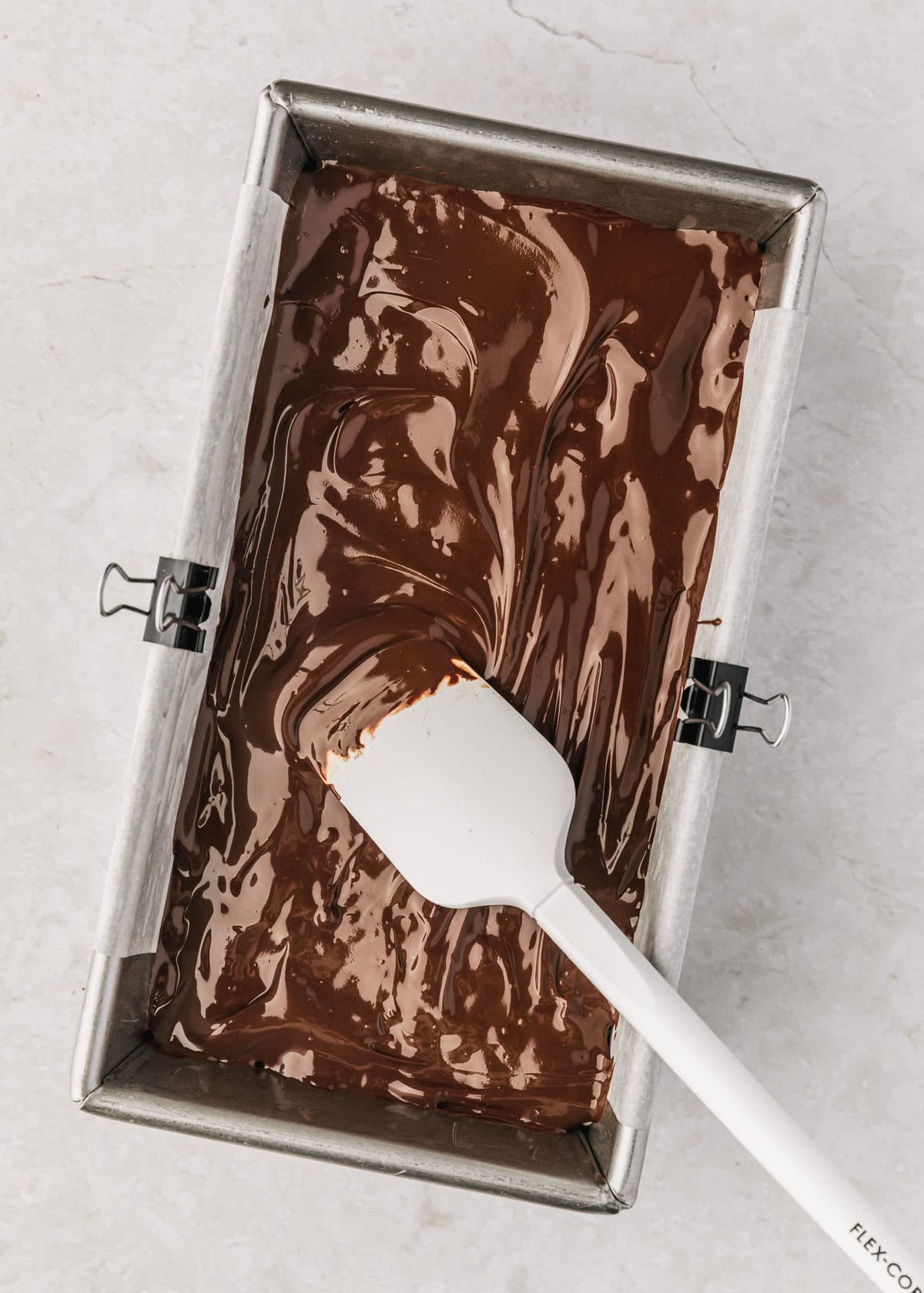 A white rubber spatula spreading chocolate on chocolate covered rice crispy treats.