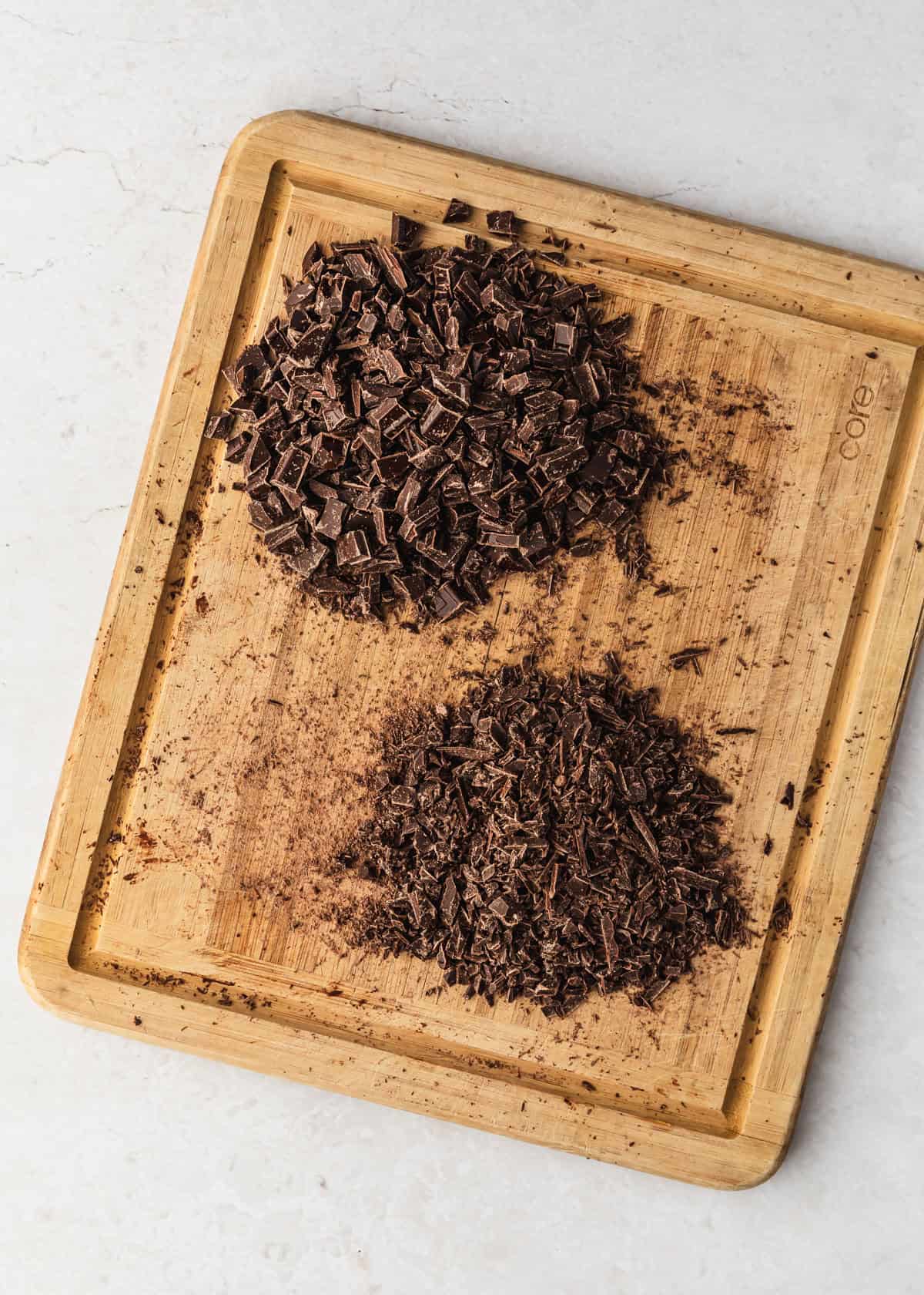 A wood board of chopped chocolate on a white counter.