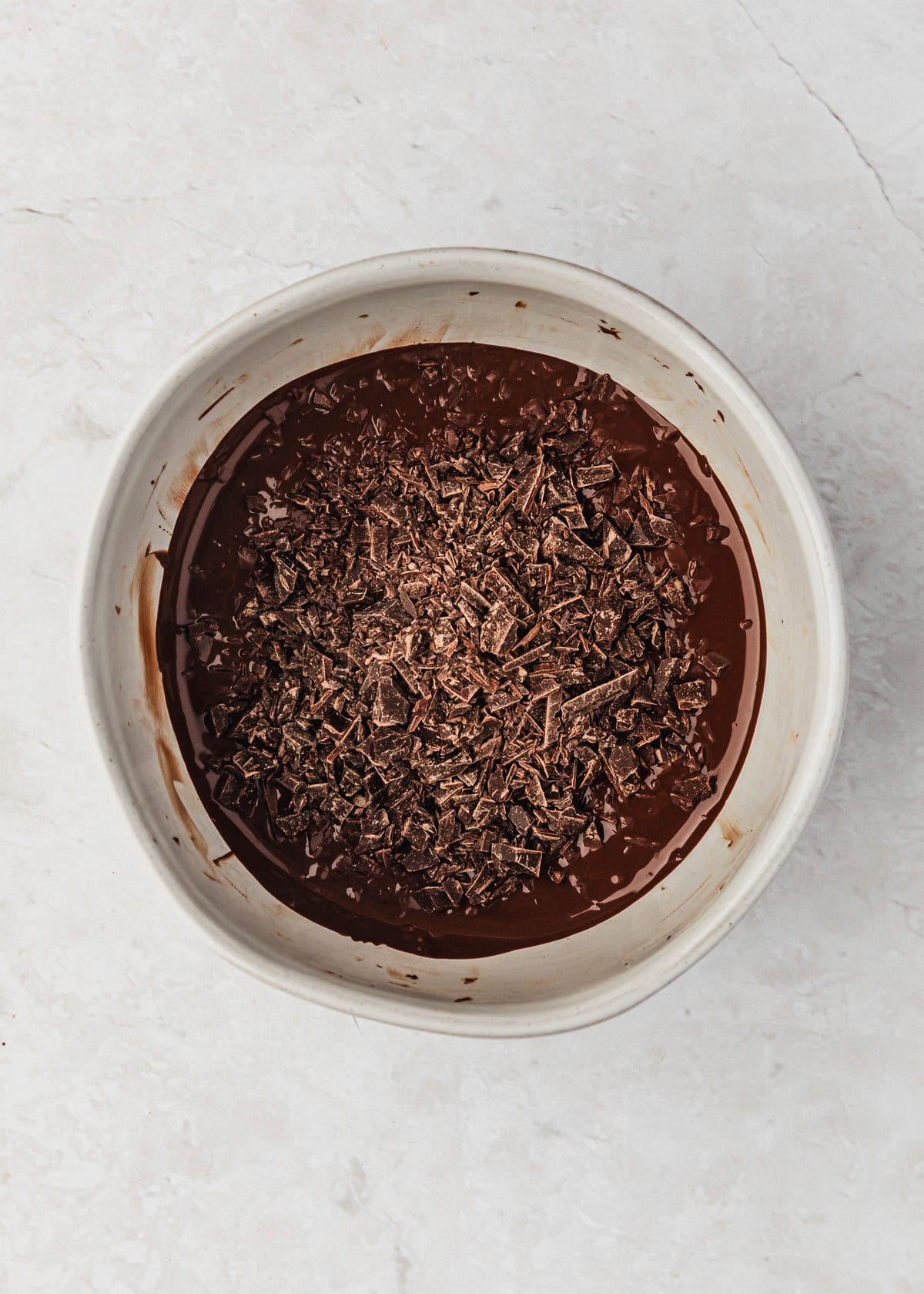 A white bowl of melted chocolate topped with chopped chocolate.