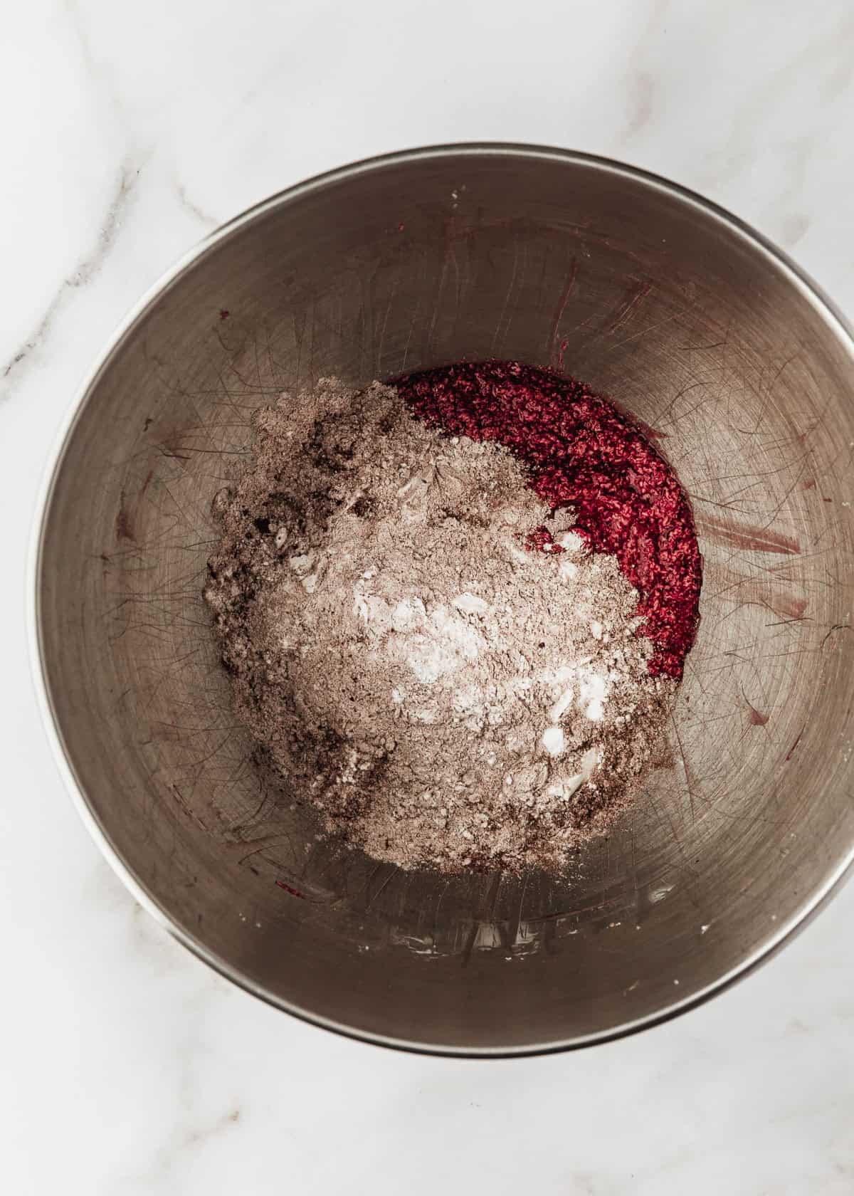 A silver bowl of beaten butter and sugar, flour, and cocoa on a white marble counter.