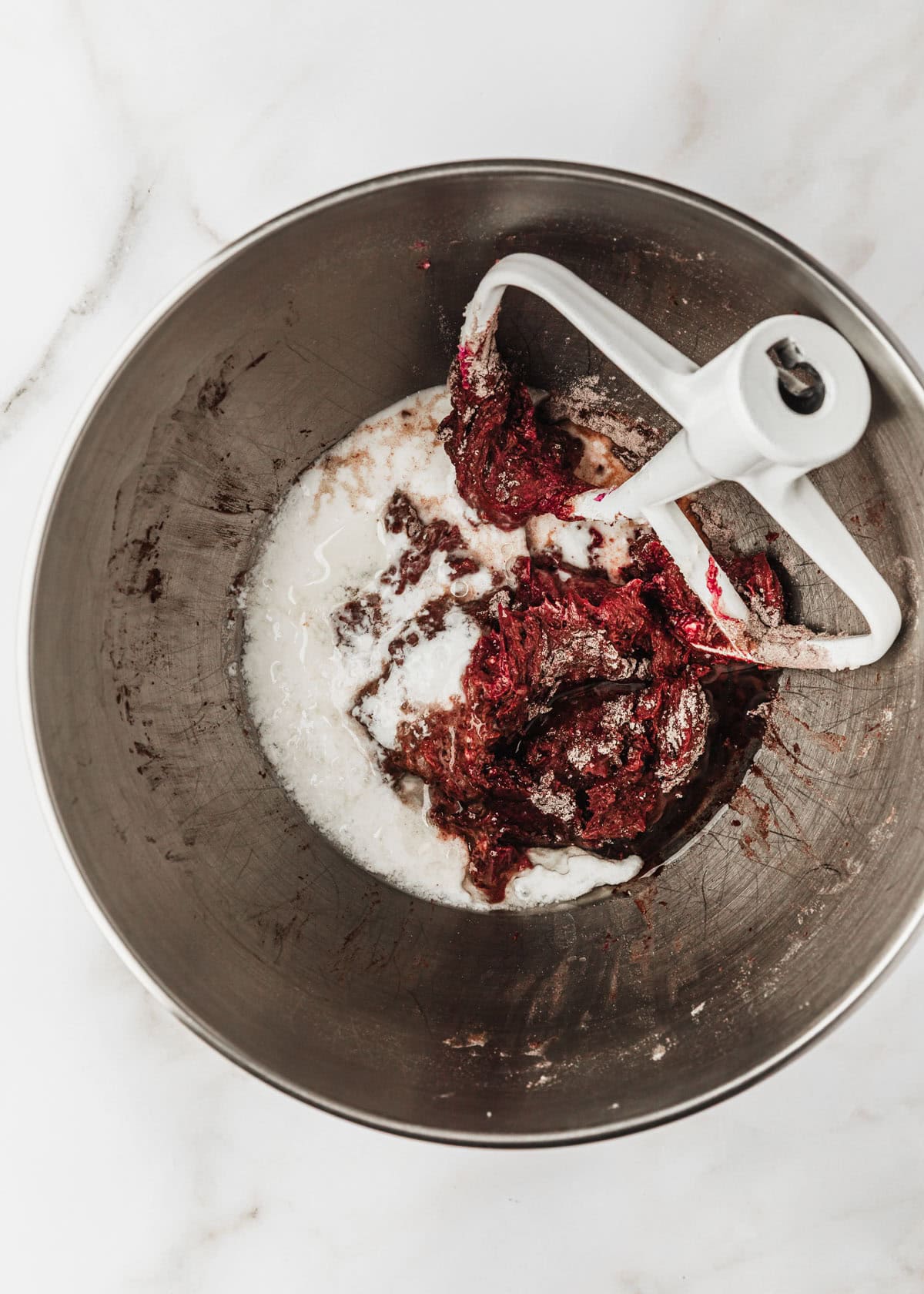 A silver bowl of red velvet cupcake batter with buttermilk.