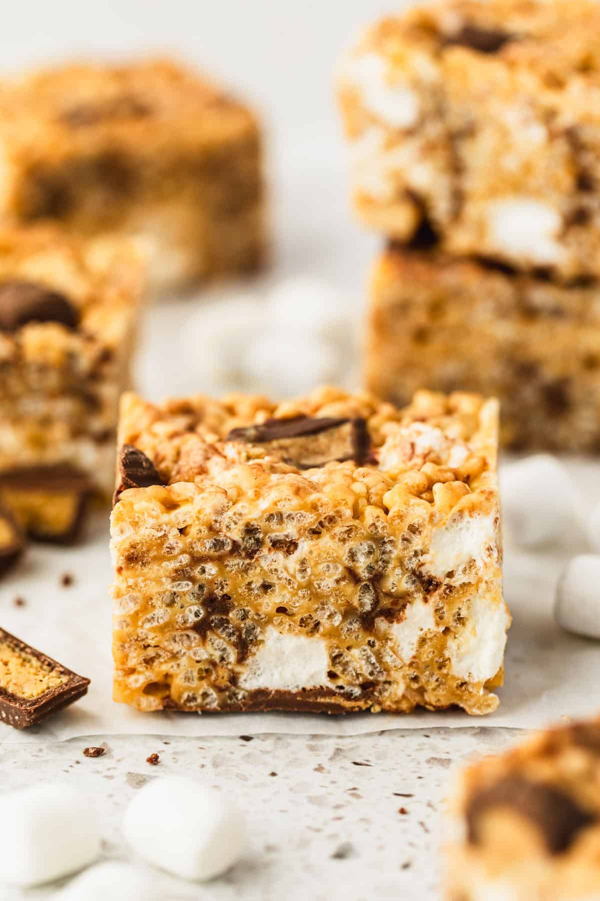 A rice krispie treat on a white counter next to stacks of small batch chocolate peanut butter rice krispie treats, marshmallows, and peanut butter cups.