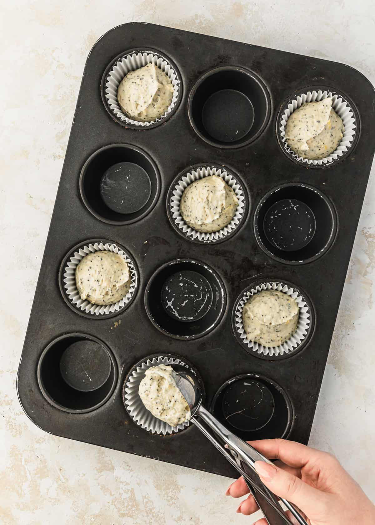A hand using a scoop to divide batter for small batch lemon poppy seed cupcakes in a cupcake pan.