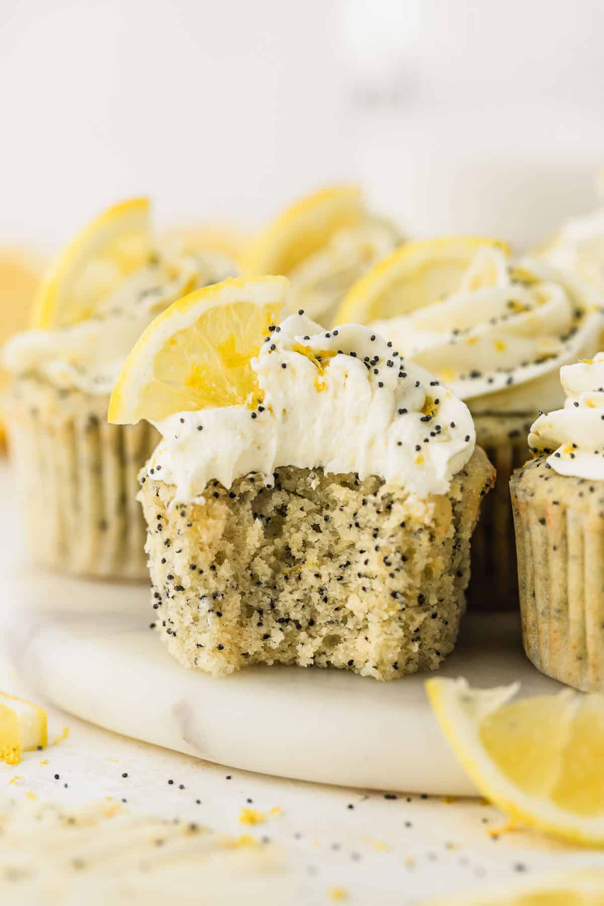 A cupcake with a bite taken out of it on a white platter of small batch lemon poppy seed cupcakes with a white background.