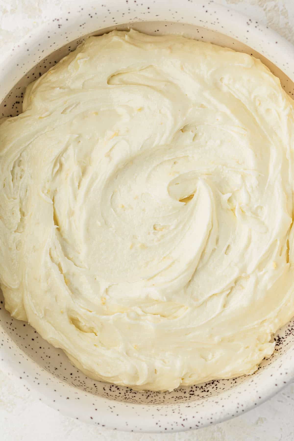 A white bowl of small batch lemon buttercream on a white counter.